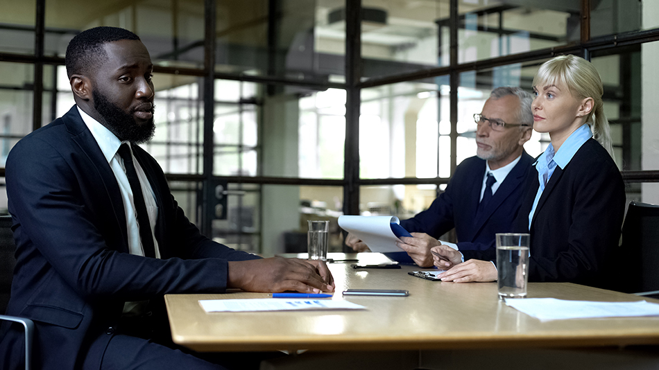 black man looking disappointed at table across from white colleagues