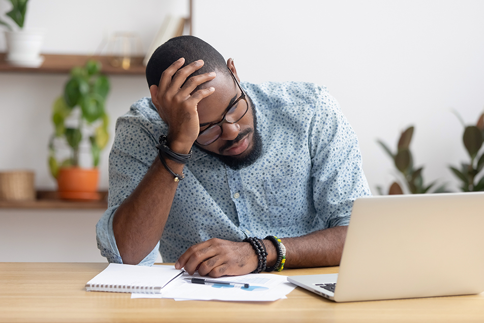 black man looking stressed in front of laptop and paperwork