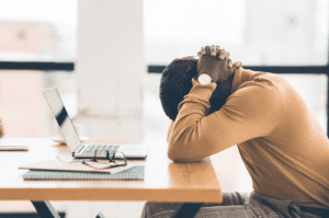 Male employee sitting with his head in his hands after having his job offer rescinded.