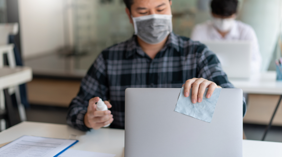 employee wearing mask and disinfecting his laptop at work