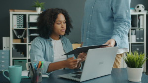 A professional employee reviews documents at an office desk with a colleague nearby, representing the federal-sector EEO complaint process and the importance of building a complete record.